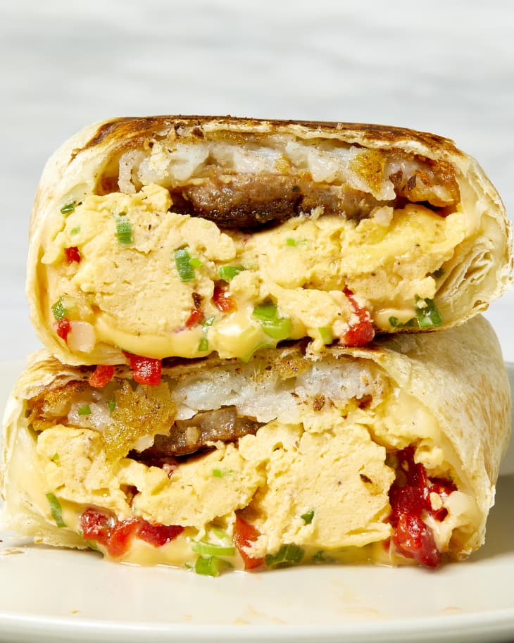Head on shot of two halves of the breakfast burrito. stacked on top of each other.  In each half you can see layers of melted cheese, scrambled eggs, sausage and hashbrowns.