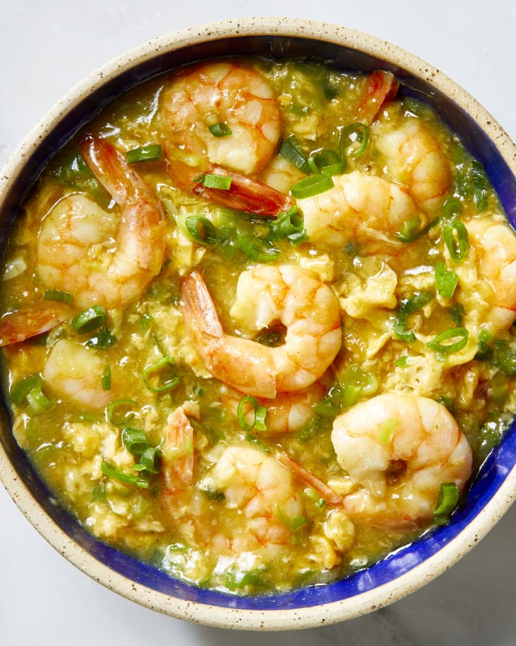 Overhead shot of shrimp with lobster sauce in a dark blue bowl, topped with green onion.