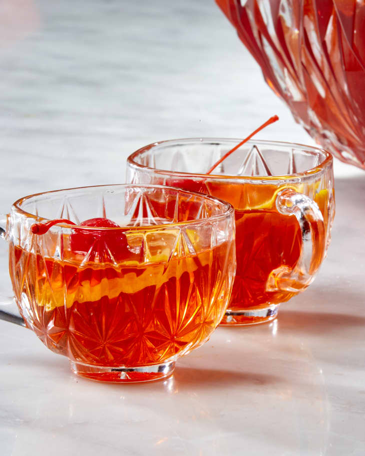 Head on shot of two punch glasses full of punch, garnished with an orange wheel and maraschino cherry.