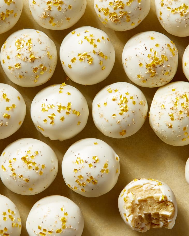 Overhead view of rows of eggnog cookie truffle topped with gold star glitter, and one with a bite taken out.