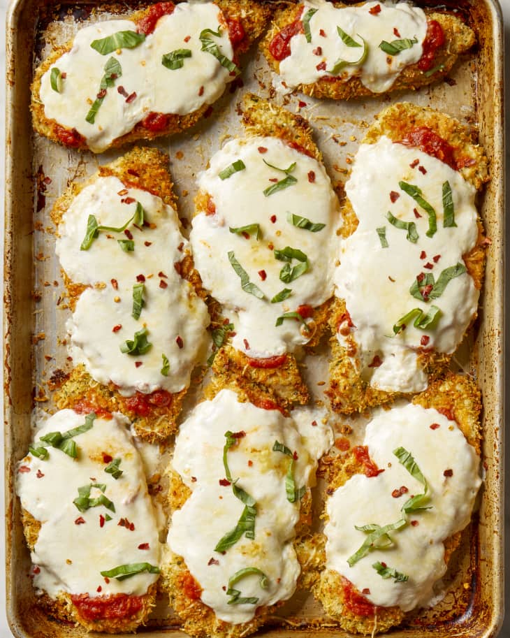 Overhead shot of baked chicken parmesan on a sheet pan, topped with red pepper flakes and basil.