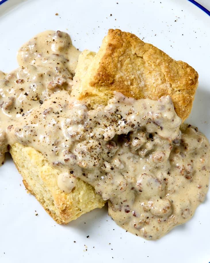 A plate with a split biscuit topped with sausage gravy and cracked black pepper.
