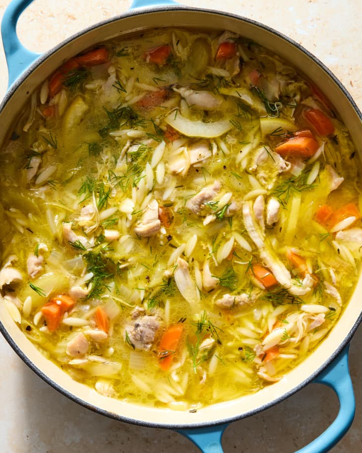 Overhead shot of chicken lemon orzo soup in a light blue pot.