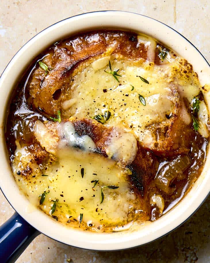 Overhead shot of french onion soup in a navy blue soup crock, topped with herbs.