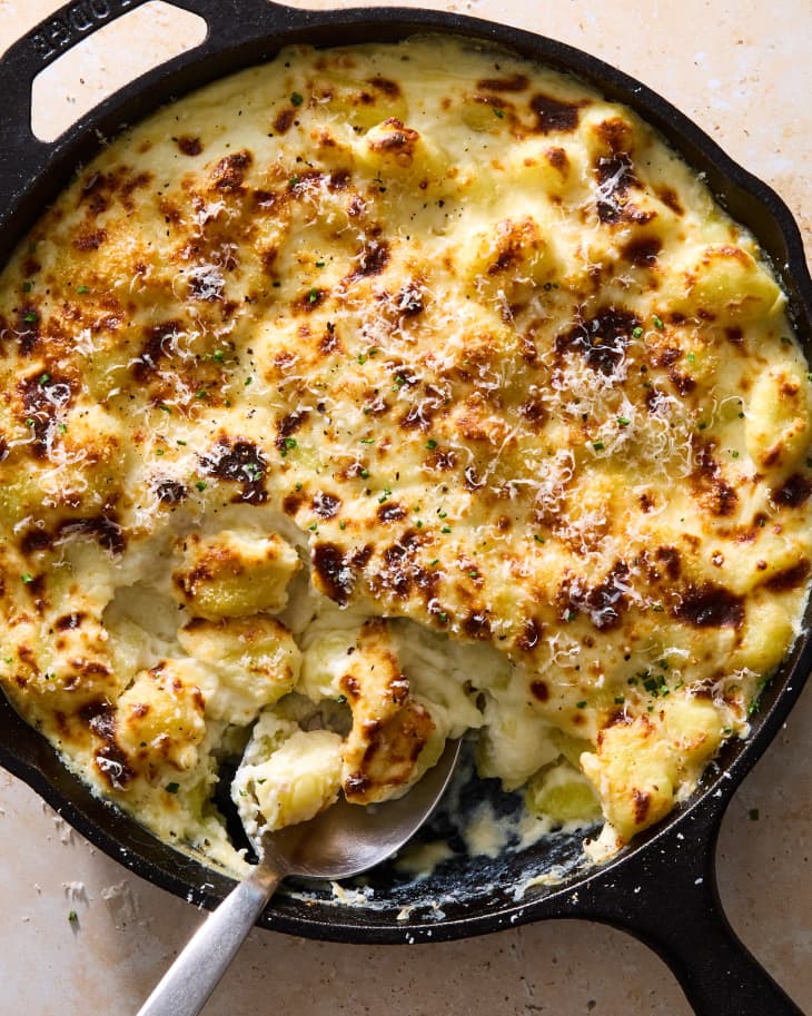 Overhead shot of the finished gnocchi alfredo bake in a black cast iron pan, topped with grated cheese and herbs.