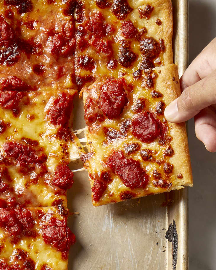 a hand reaching in and pulling out a slices of pizza from the sheet pan.