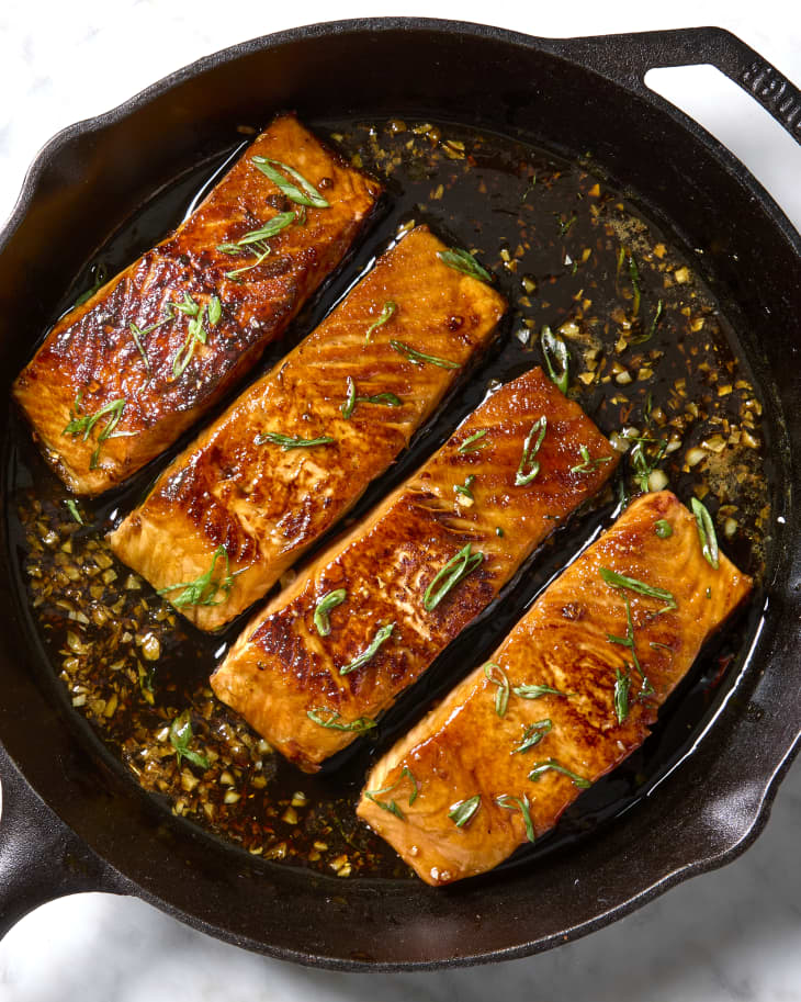 Overhead shot of four cooked pieces of salmon in a cast iron, topped with green onion.