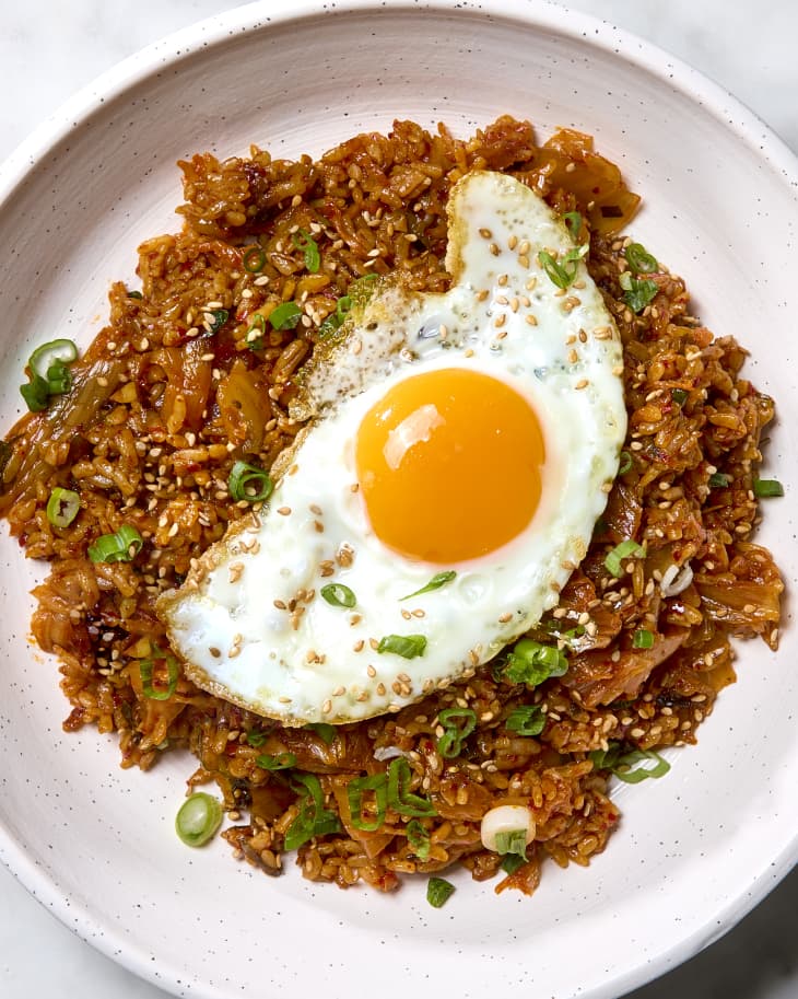 Overhead shot of kimchi fried rice in a shallow light pink bowl, topped with a fried egg and green onion.