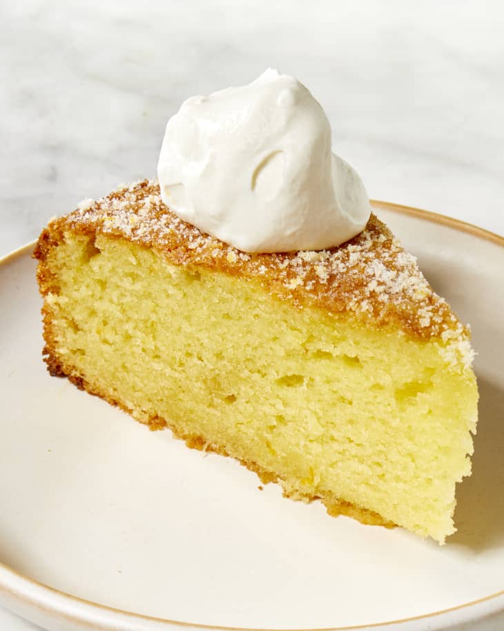 Angled shot of a slice of olive oil cake topped with whipped cream.
