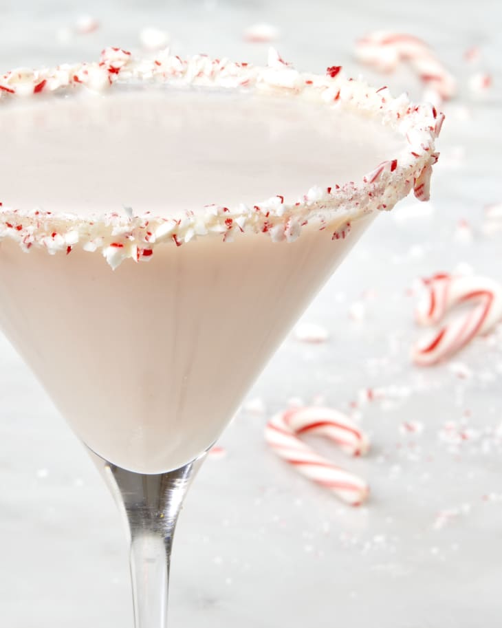 Close up head on shot of a peppermint martini with a candy cane rim and broken candy cane pieces in the background of the shot.