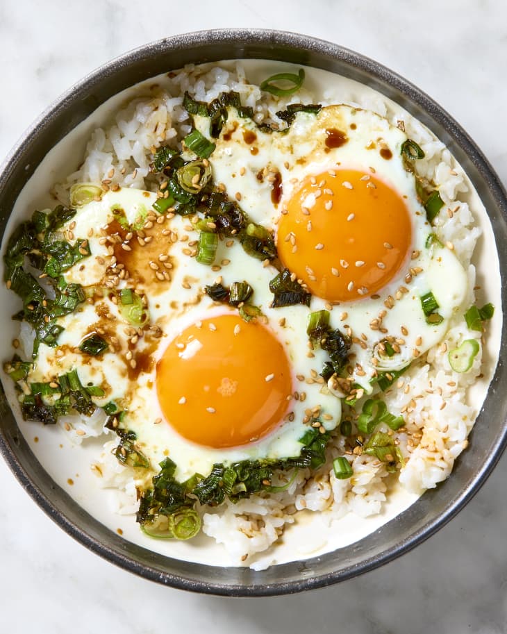 Overhead shot of two fried eggs with scallions in a bowl over rice, topped with sesame seeds.