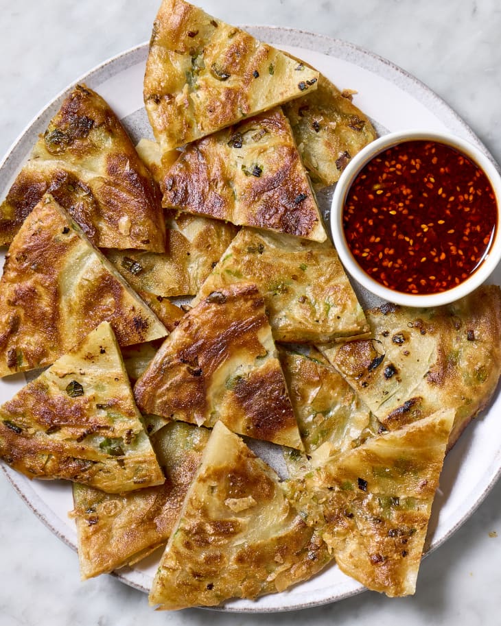 Cut scallion pancakes on a serving plate with a chili dipping sauce.