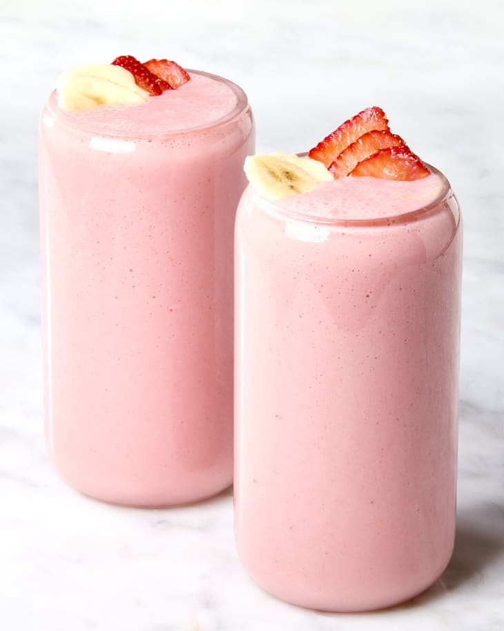 Head on shot of two glasses filled with strawberry banana smoothie in them, and garnished with sliced strawberries and bananas.
