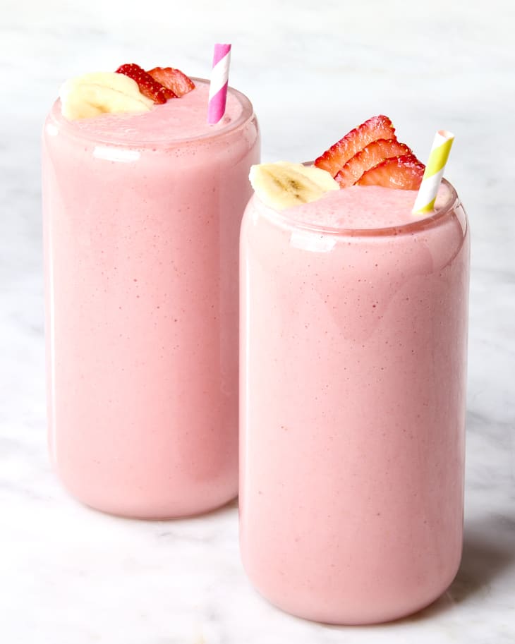 Head on shot of two glasses filled with strawberry banana smoothie in them, and garnished with sliced strawberries and bananas.