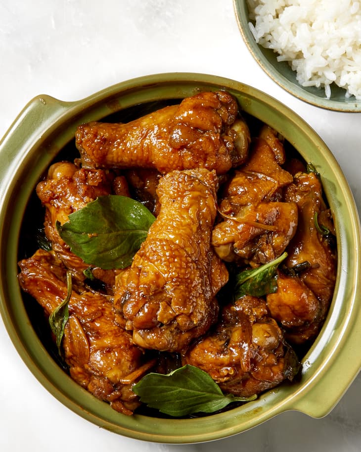 Overhead shot of three cup chicken served in a green bowl and a small bowl full of rice on the side.