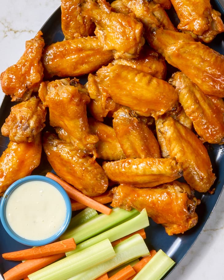 overhead shot of buffalo wings on a dark blue plate with carrot and celery sticks, with a small cup of ranch.