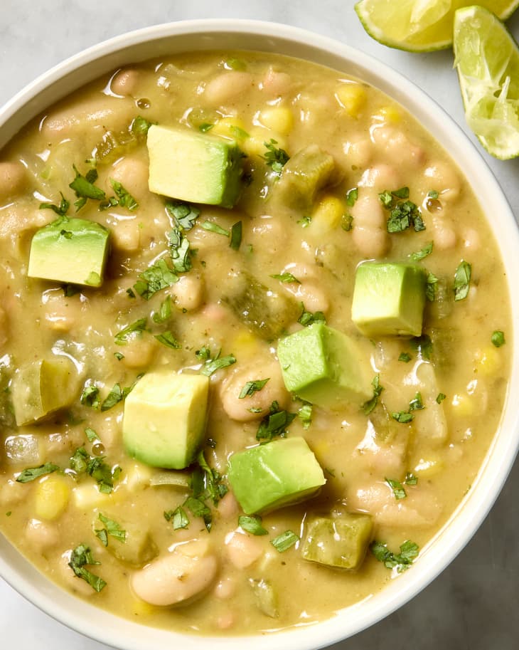 overhead shot of a bowl of creamy white bean chili topped with herbs and avocado.