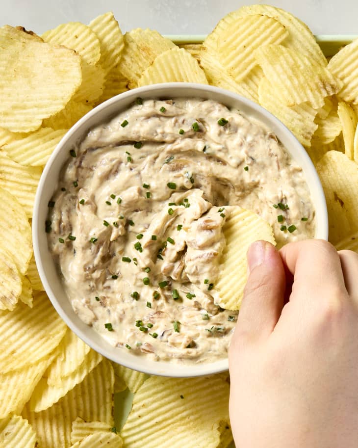 overhead shot of a hand dipping a potato chip into the french onion dip.