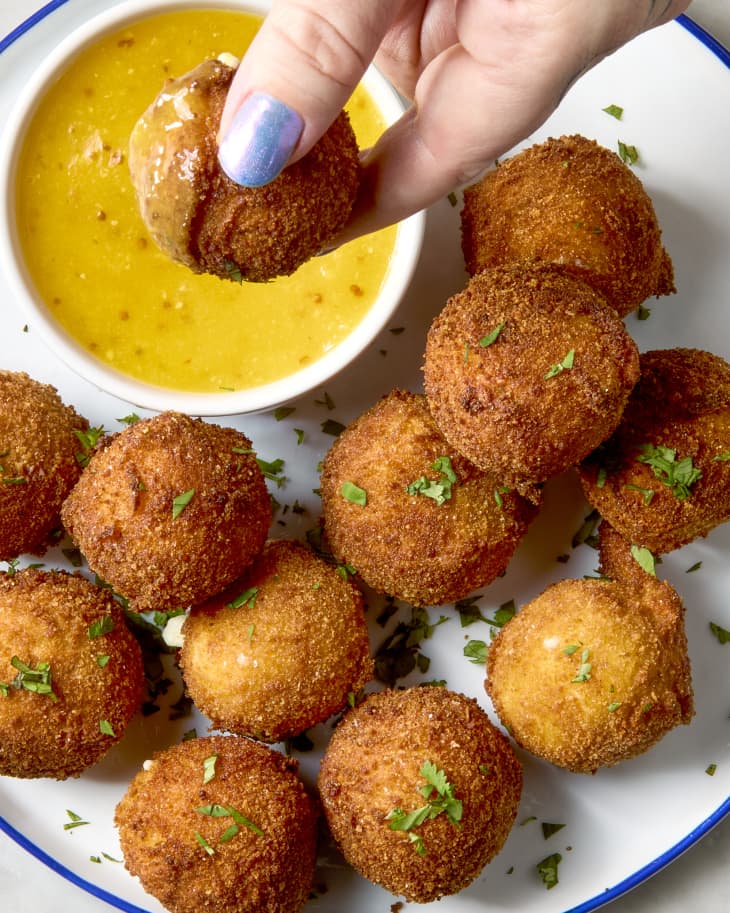 overhead shot of a hand dipping a fried goat cheese ball into the side of mustard sauce.