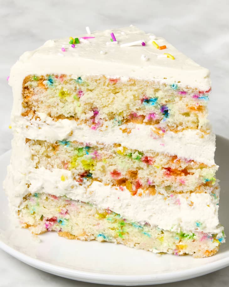head on shot of a slice of the funfetti cake, with vanilla frosting and topped with rainbow sprinkles.