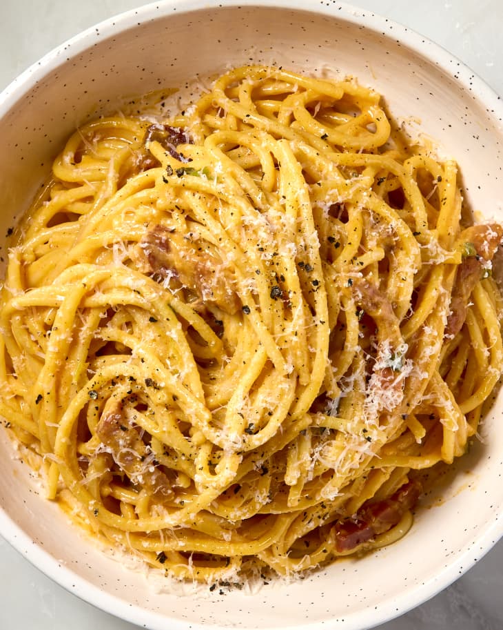 overhead shot of gochujang carbonara in a small speckled bowl, topped with fresh black pepper and cheese.