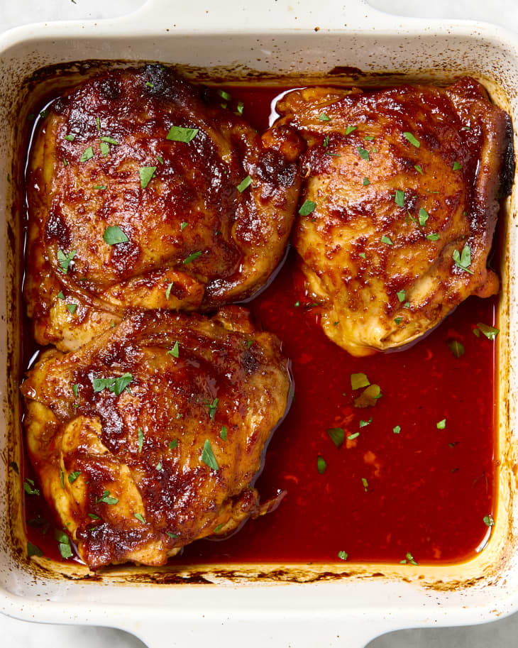 overhead shot of three harissa orange chicken thighs in a small white baking dish.