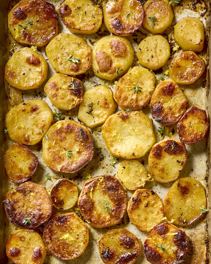 overhead shot of lemon butter potatoes on a baking sheet, topped with herbs.