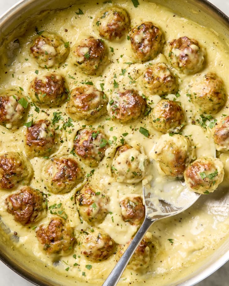 overhead shot of creamy lemon pepper chicken meatballs in a metal skillet, with a large serving spoon resting in the pan with a couple meatballs on it..