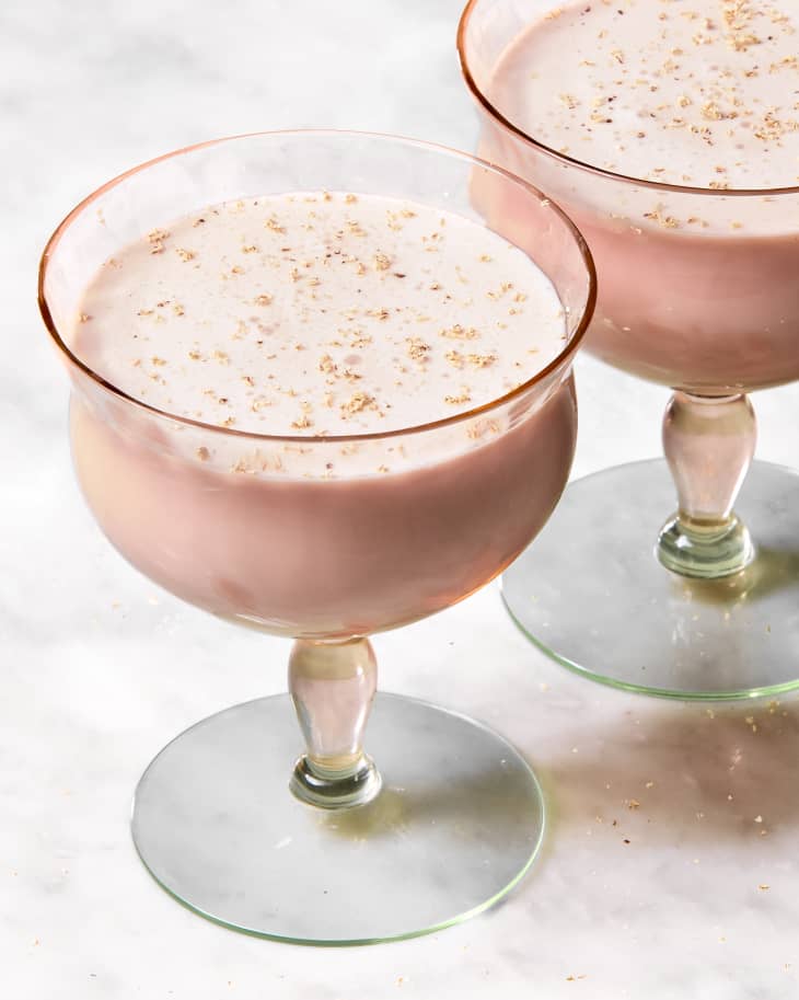 angled shot of two glasses of the pink squirrel cocktail on a marble surface, topped with shaved nutmeg.