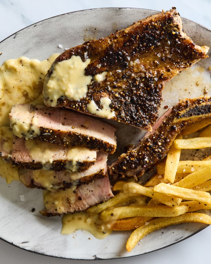 overhead shot of pork chop au poivre, partially sliced on a grey plate with fries.
