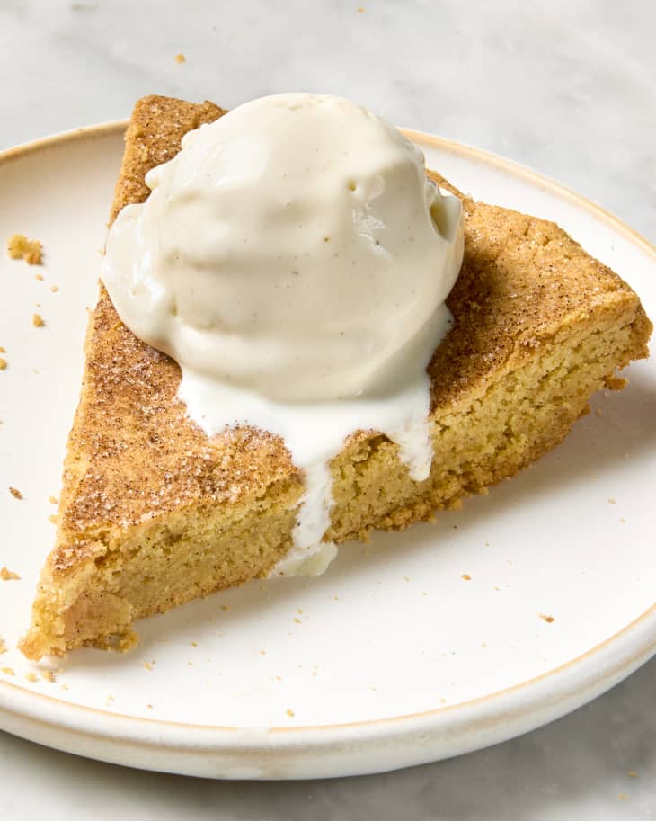 angled shot of a slice of the snickerdoodle skillet cookie on a small white plate, with a scoop of vanilla ice cream on top.