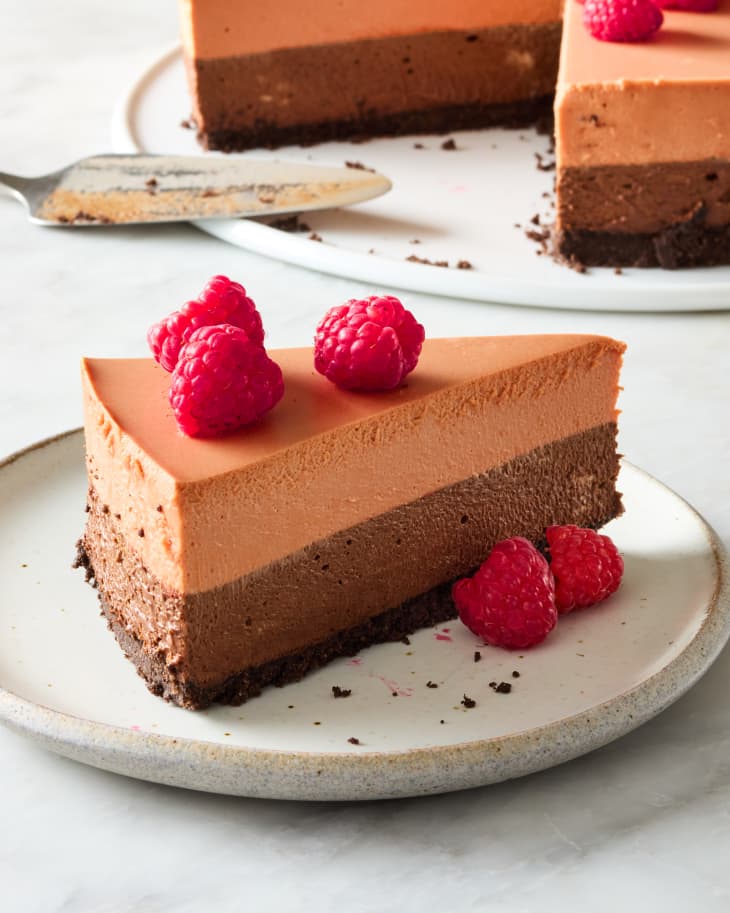 angled shot of a piece of triple chocolate mousse cake topped with raspberries.