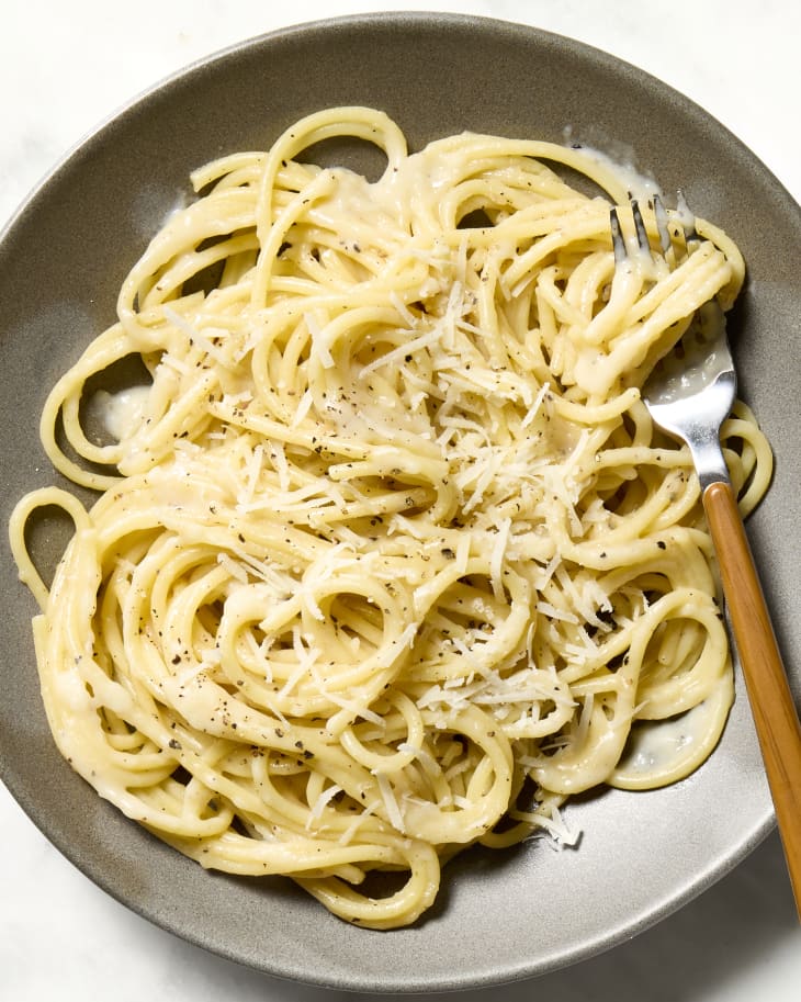 overhead shot of cacio e pepe on a grey plate, with a fork resting on the edge of the plate.