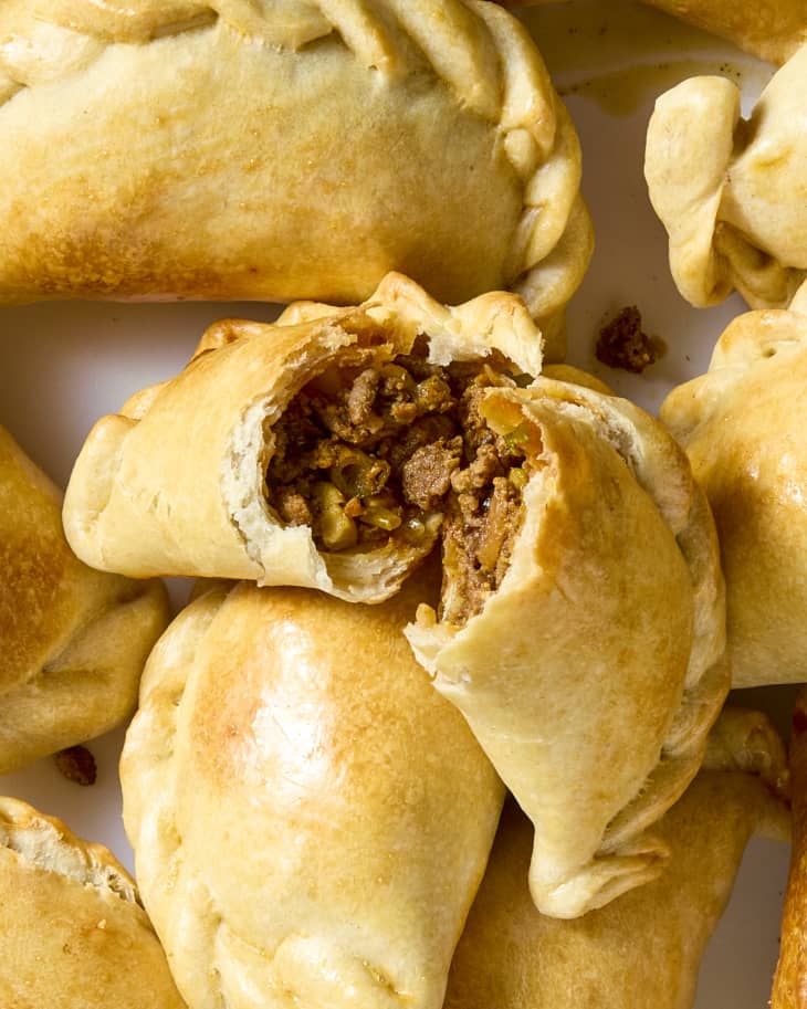 overhead shot of cooked empanadas on a plate, with one broken open.