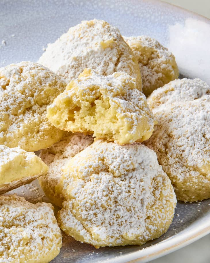 overhead shot of a pile of lemon cloud cookies on a white plate with one bitten into.