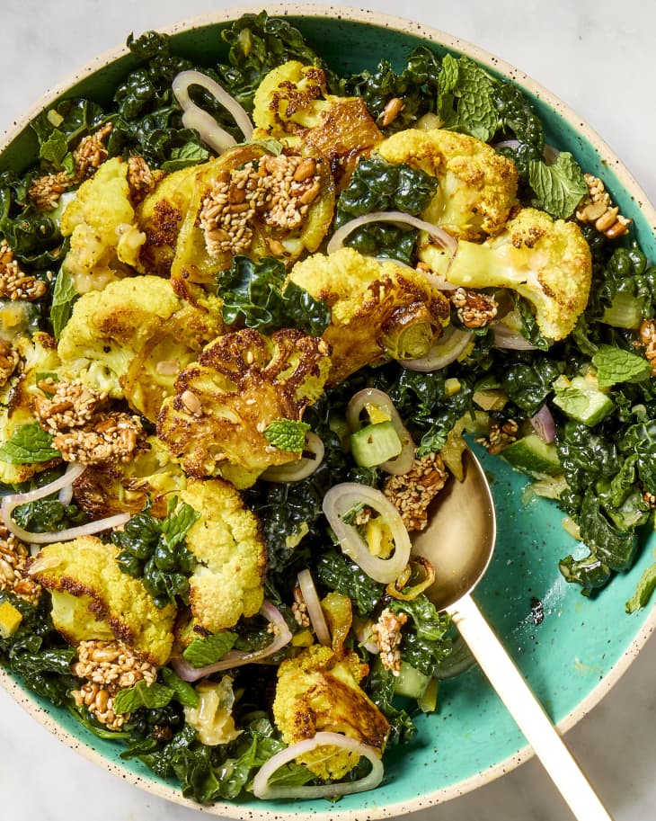 overhead shot of a roasted cauliflower salad in a teal bowl, with a scoop taken from it.