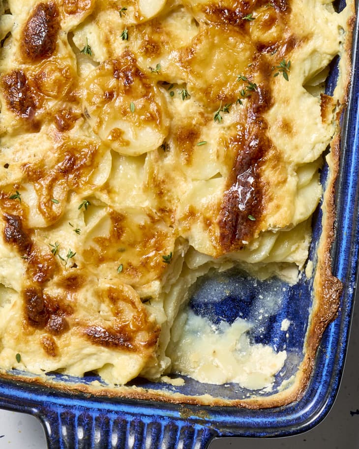 overhead shot of scalloped potatoes in a dark blue baking dish, with a large scoop taken from the bottom right corner.