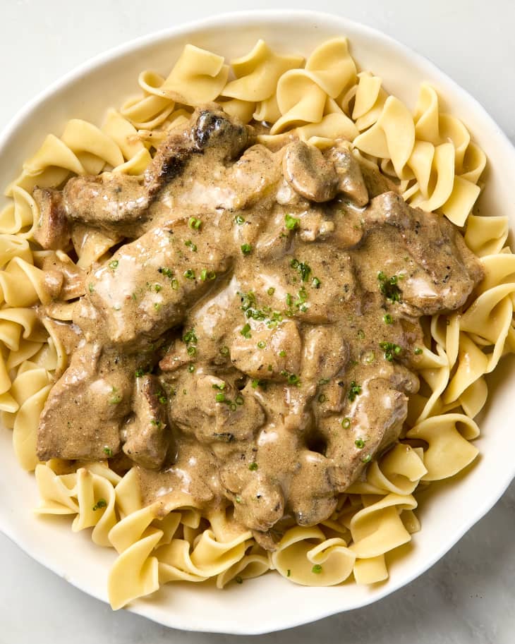 overhead shot of beef stroganoff being served over egg noodles in a white bowl.