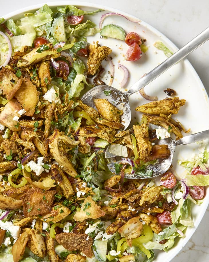 overhead shot of chicken shawarma salad on a white serving plate, with two salad tongs resting on the plate.