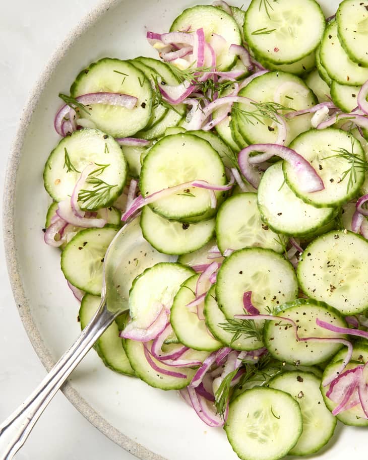overhead shot of cucumber salad in a large white salad bowl, with a spoon resting in the bowl