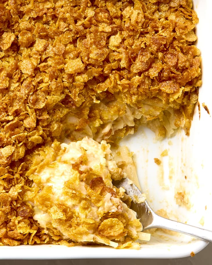 overhead shot of funeral potatoes in a white casserole dish, with a large scoop out of the bottom right corner.