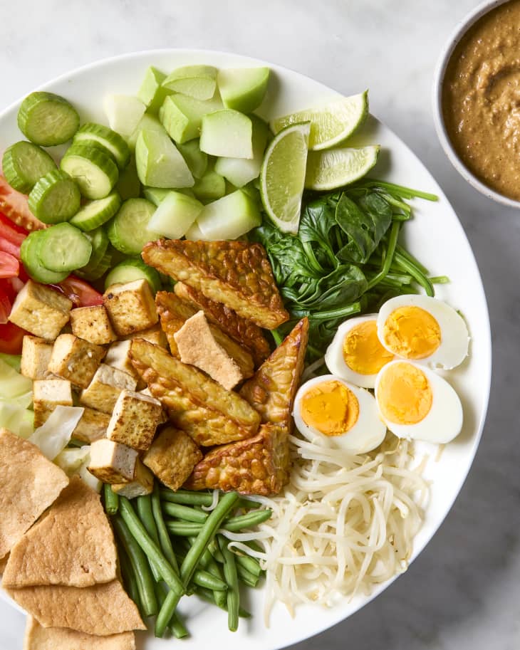 overhead shot of fully constructed gado gado in a large white bowl, with a side of peanut dressing.