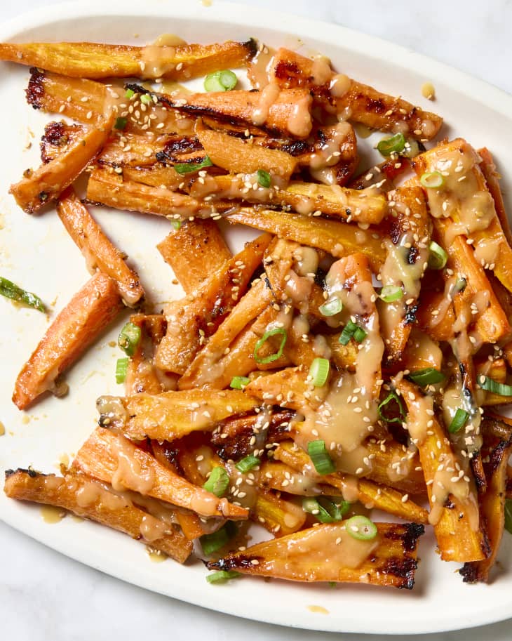 overhead shot of miso butter glazed carrots on a white platter, topped with white sesame seeds and green onion.