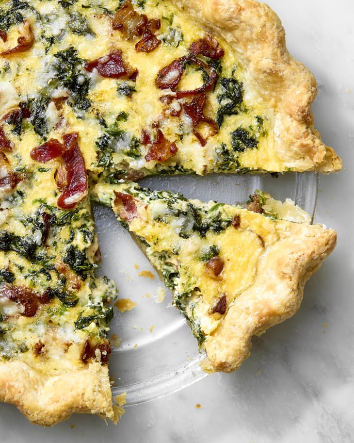 overhead shot of a partially cut quiche, with a slice resting in the clear pie pan.