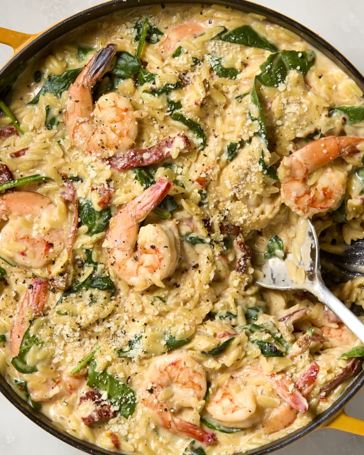 overhead shot of tuscan shrimp orzo in a yellow pan, topped with parmesan cheese.