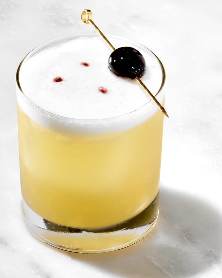 angled shot of a single whiskey sour, garnished with a luxardo cherry.