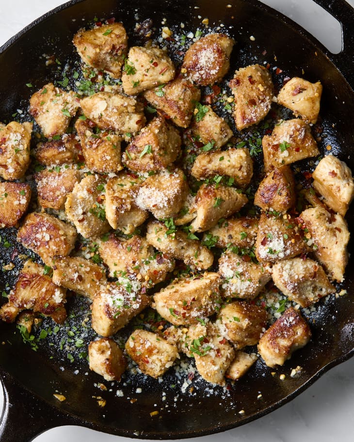 An overhead shot of chicken garlic parmesan bites in a cast iron skillet on a marble surface