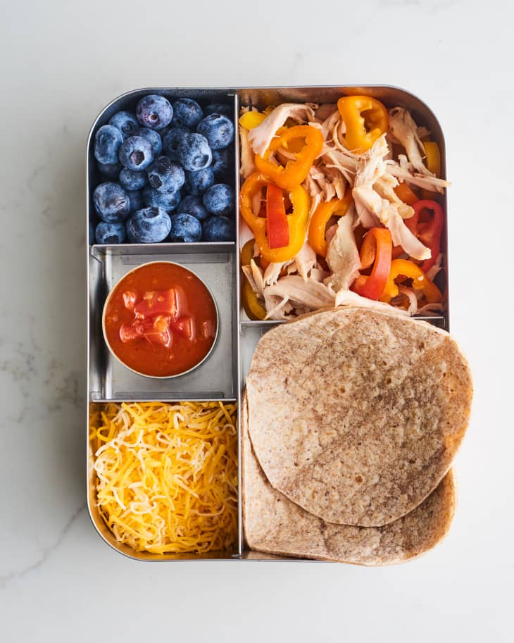 Lunchbox with blueberries, shredded chicken, bell peppers, salsa, shredded cheese, and whole wheat tortillas.