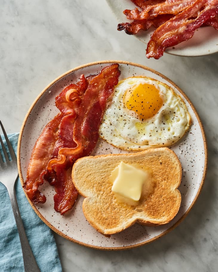 Plate with strips of bacon, a fried egg, and a piece of toast with melting pat of butter