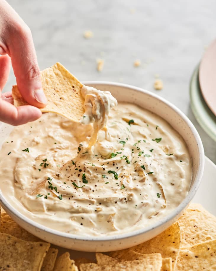 hand dipping chip into a bowl of caramelized onion dip